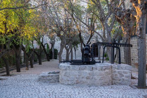 Free A peaceful courtyard in warm evening light featuring an old stone well surrounded by bare trees. Stock Photo