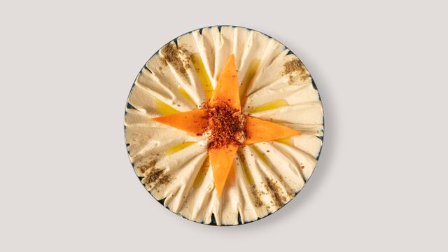 Artistic hummus dish topped with paprika, oil, and spices, styled in a star shape.