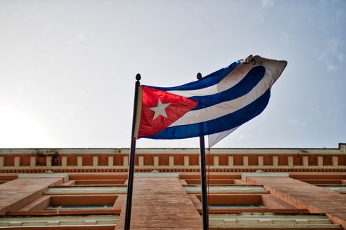 Free Cuban flag waving against a historic building in Havana, capturing national pride and architectural beauty. Stock Photo