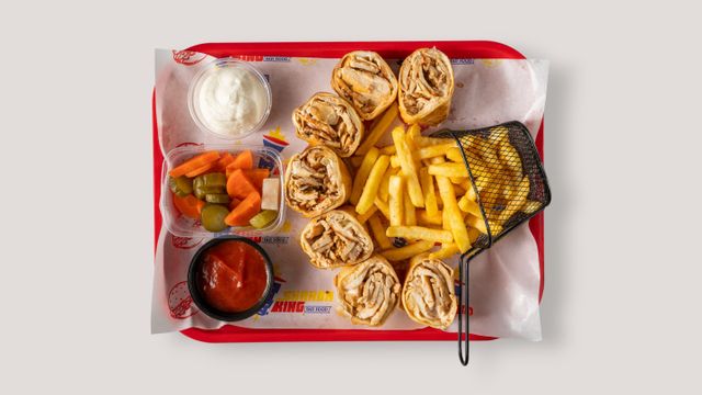 Flat lay of a fast food platter with shawarma, french fries, dips, and pickles.