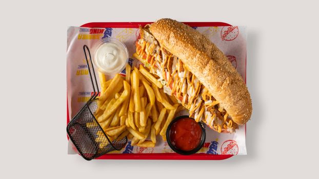 Mouth-watering sub sandwich served with crispy fries and two tasty sauces on a tray.