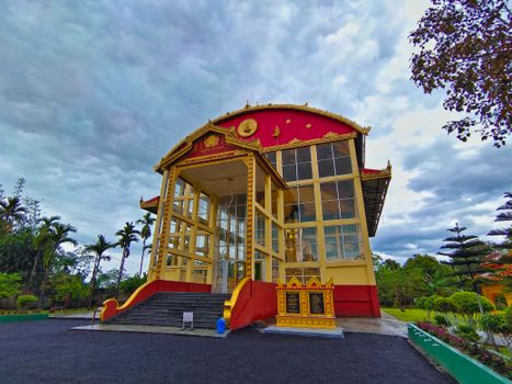 Colorful traditional building with ornate details set amidst lush greenery during a cloudy day.