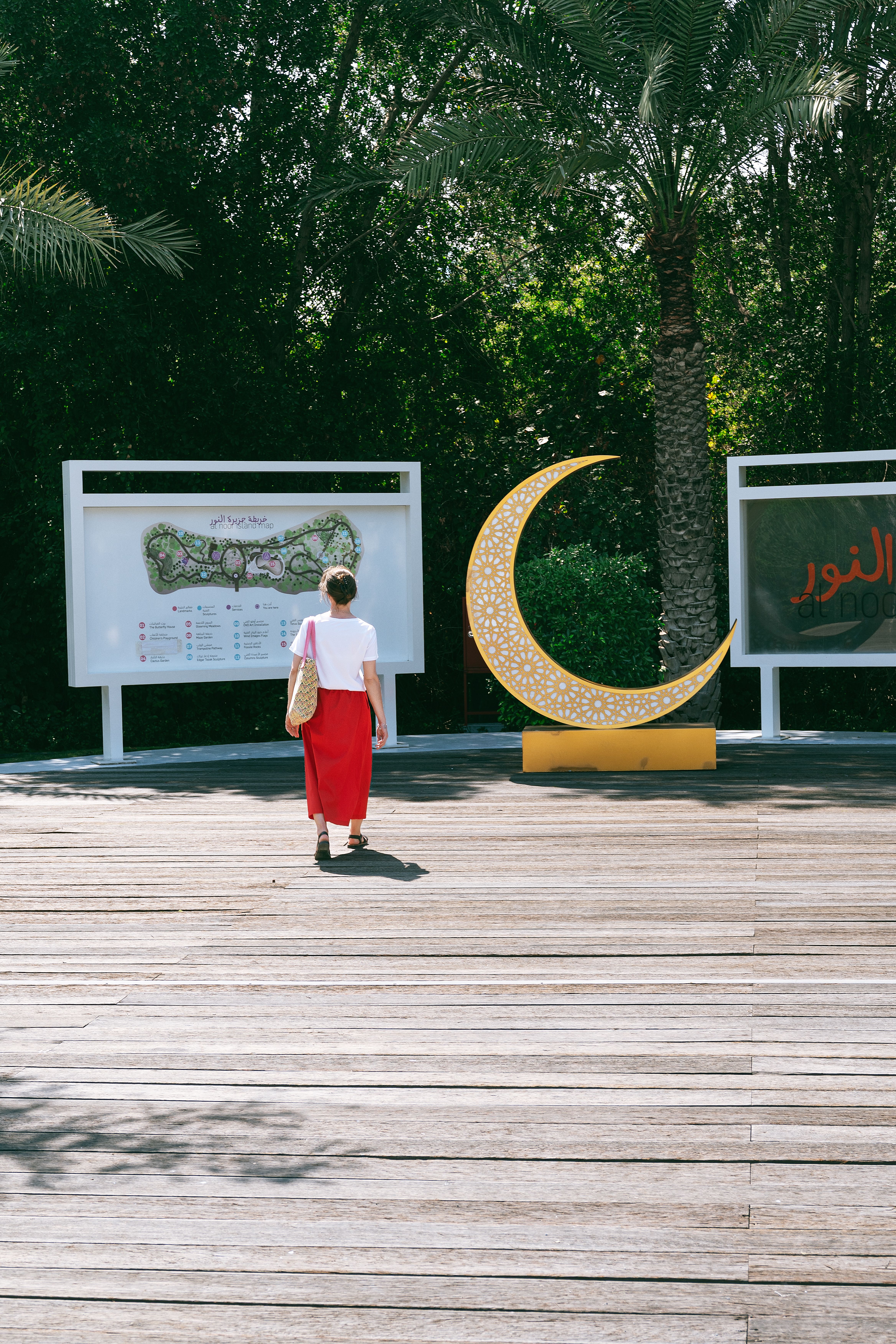 A woman in red walks towards a crescent sculpture in Al Noor Island, Sharjah.