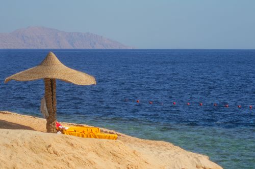 Free Serene beach with a straw parasol, sandy shore, and clear blue sea under a sunny sky. Stock Photo