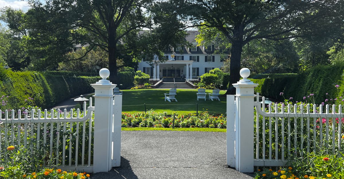 A picturesque view of a mansion garden with a white fence, vibrant flowers, and lush greenery.