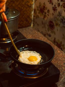 A sunny side up egg frying in a pan on a stovetop with floral wallpaper in an Indian kitchen.