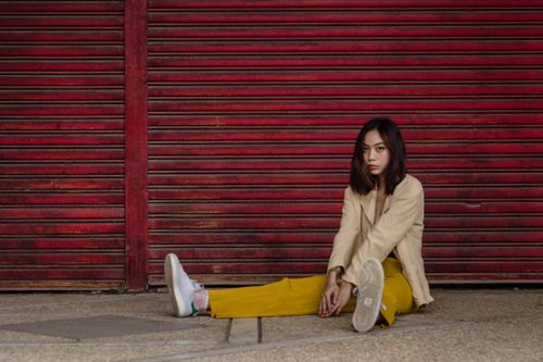 Free Stylish woman in casual attire sitting against a red shutter, showcasing modern fashion and unique style. Stock Photo