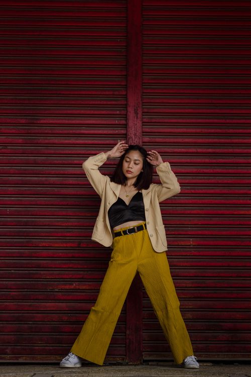Free Woman in bold outfit posing stylishly against a vibrant red wall. Stock Photo