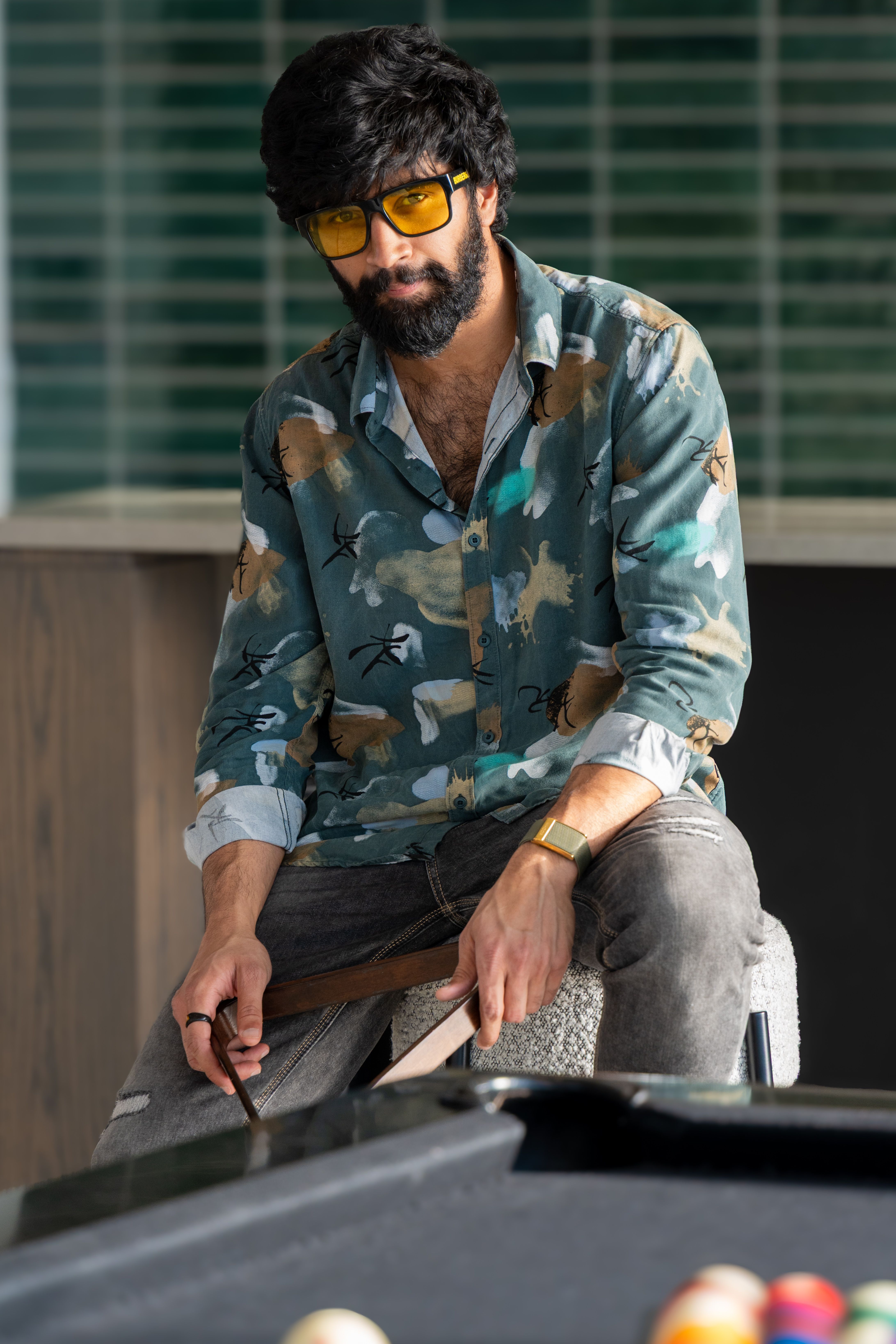 Man with beard and sunglasses playing pool in a casual setting.