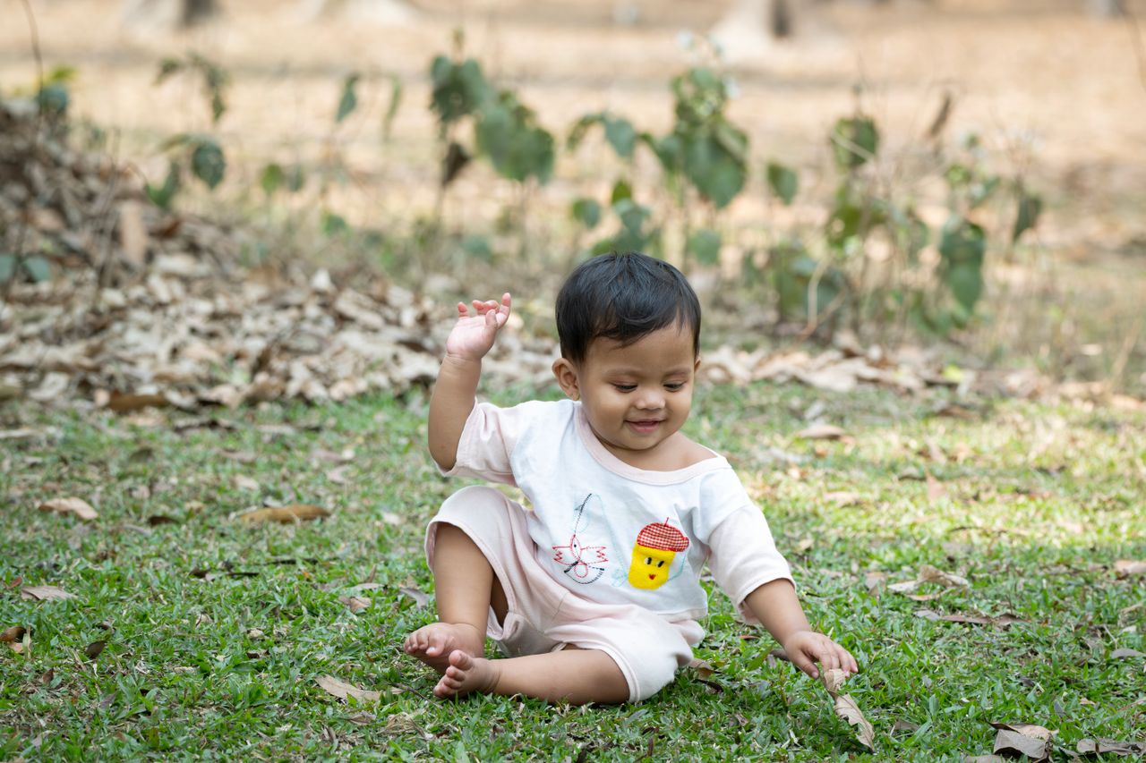 a smiling baby sitting on grass enjoying playtime in a sunny park sett