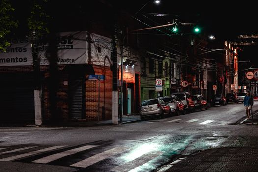 A quiet urban street at night with parked cars and wet reflections under streetlights.