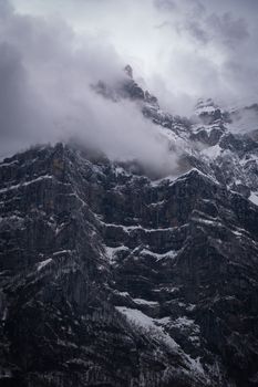 A breathtaking view of a snow-covered mountain peak enveloped in fog and clouds, creating a dramatic scene.