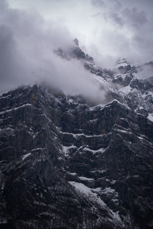 Free A breathtaking view of a snow-covered mountain peak enveloped in fog and clouds, creating a dramatic scene. Stock Photo