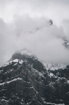 A striking view of a snow-covered mountain peak shrouded in mist and clouds, creating a moody atmosphere.
