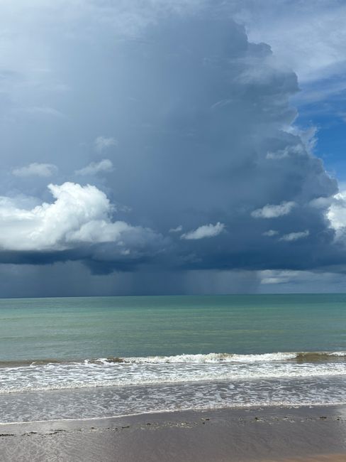 Photo by Edmo Ferrão Majestic storm clouds gathering over the ocean at a tropical beach, with waves gently hitting the shore.