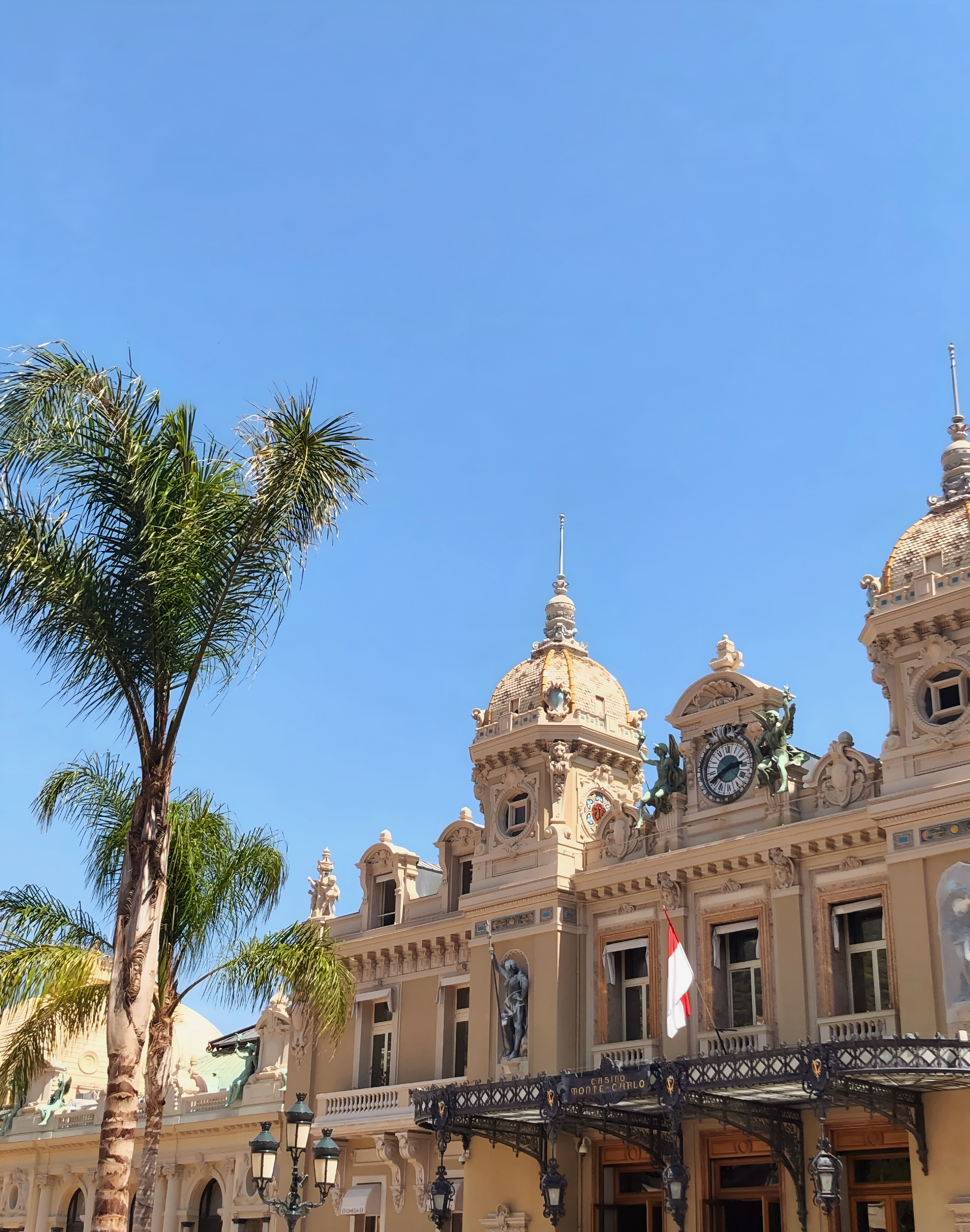 A stunning view of the iconic Monte Carlo Casino with clear blue skies and palm tree in Monaco.