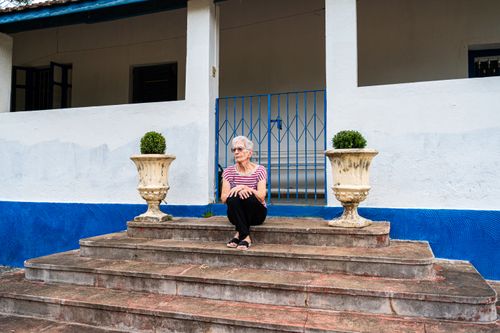 Free Elderly woman sitting on concrete steps with blue railing and rustic planters. Stock Photo