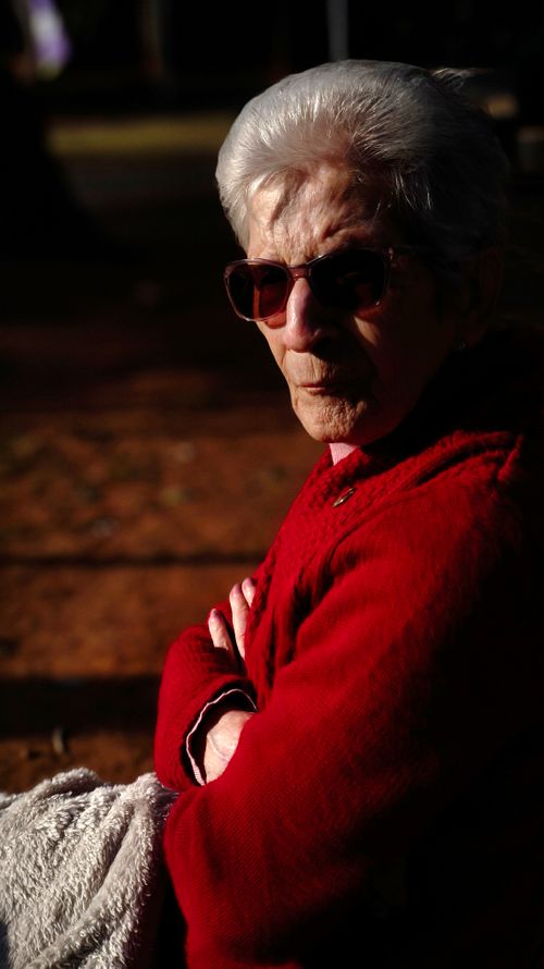 Free Senior woman enjoying a sunny day in the park, dressed warmly and wearing sunglasses. Stock Photo