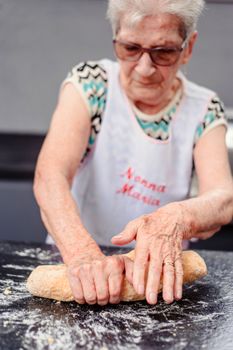 Senior woman rolling bread dough on a kitchen countertop, showcasing traditional baking skills.
