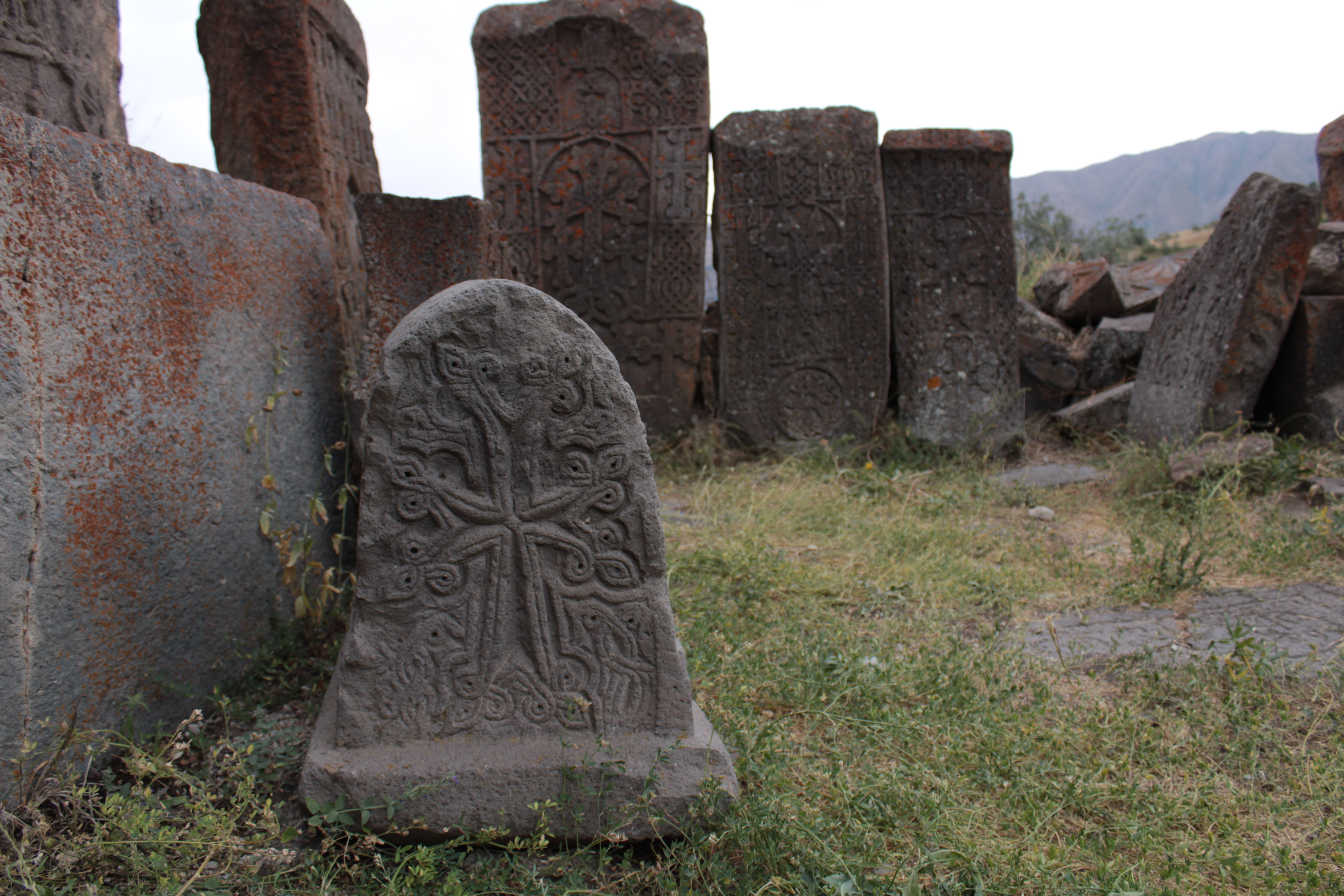 Detailed view of an ornate khachkar in an Armenian cemetery amidst historical stone slabs. (Photo by Andranik Paradyan on Pexels)