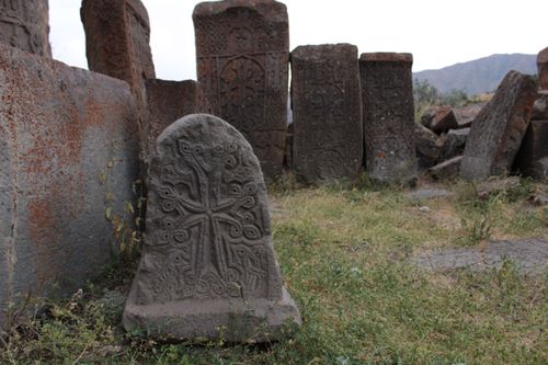 Free Detailed view of an ornate khachkar in an Armenian cemetery amidst historical stone slabs. Stock Photo