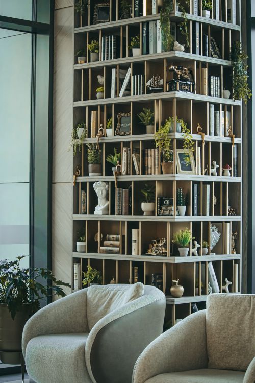Free A modern lounge featuring a unique bookshelf filled with books and decorative plants, creating a cozy atmosphere. Stock Photo