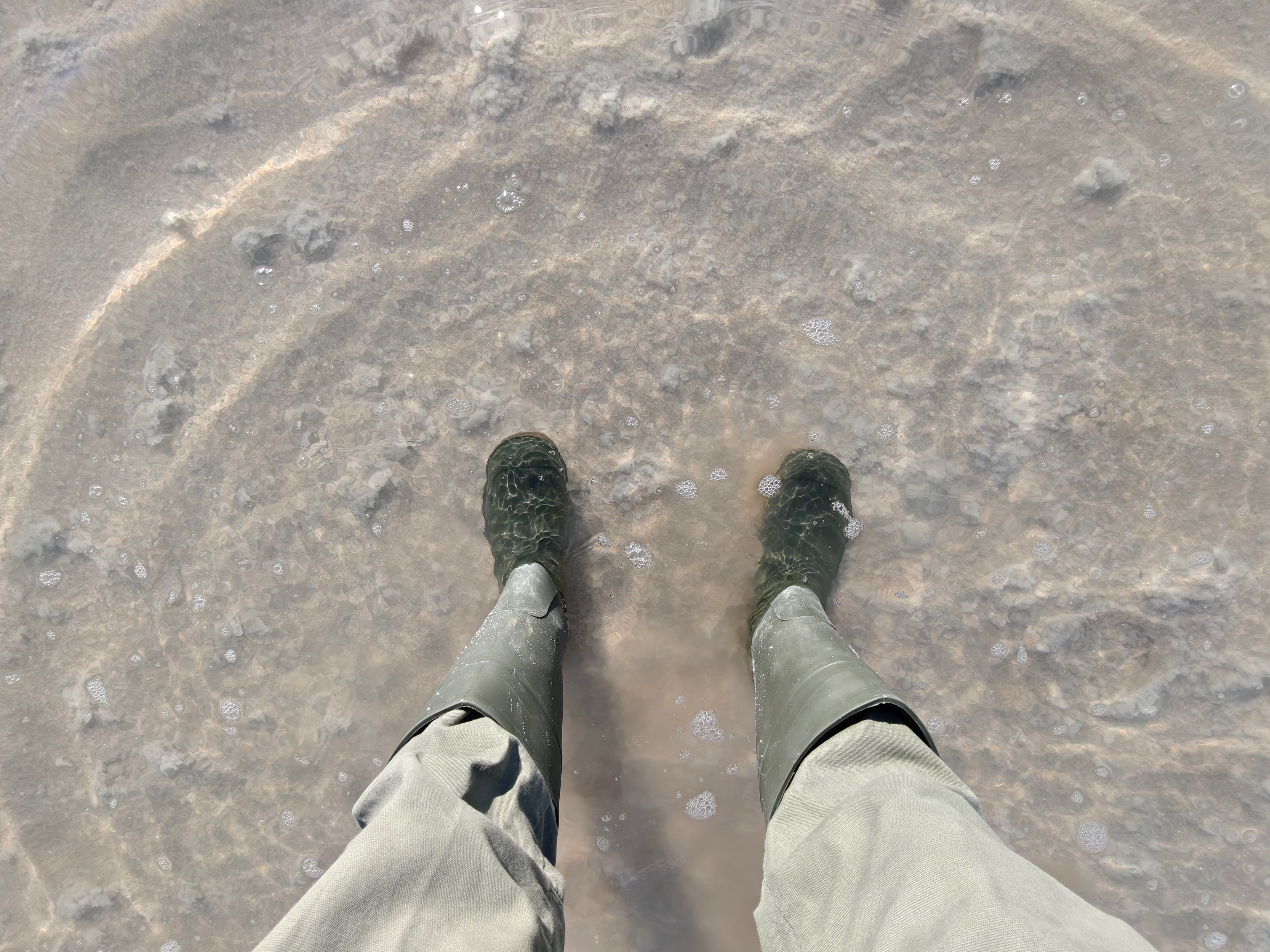 A person in boots stands in a shallow, salt-filled water area in Death Valley, California.