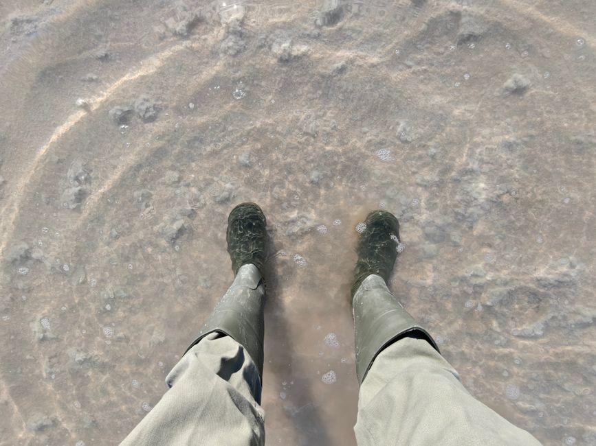 A person in boots stands in a shallow, salt-filled water area in Death Valley, California.