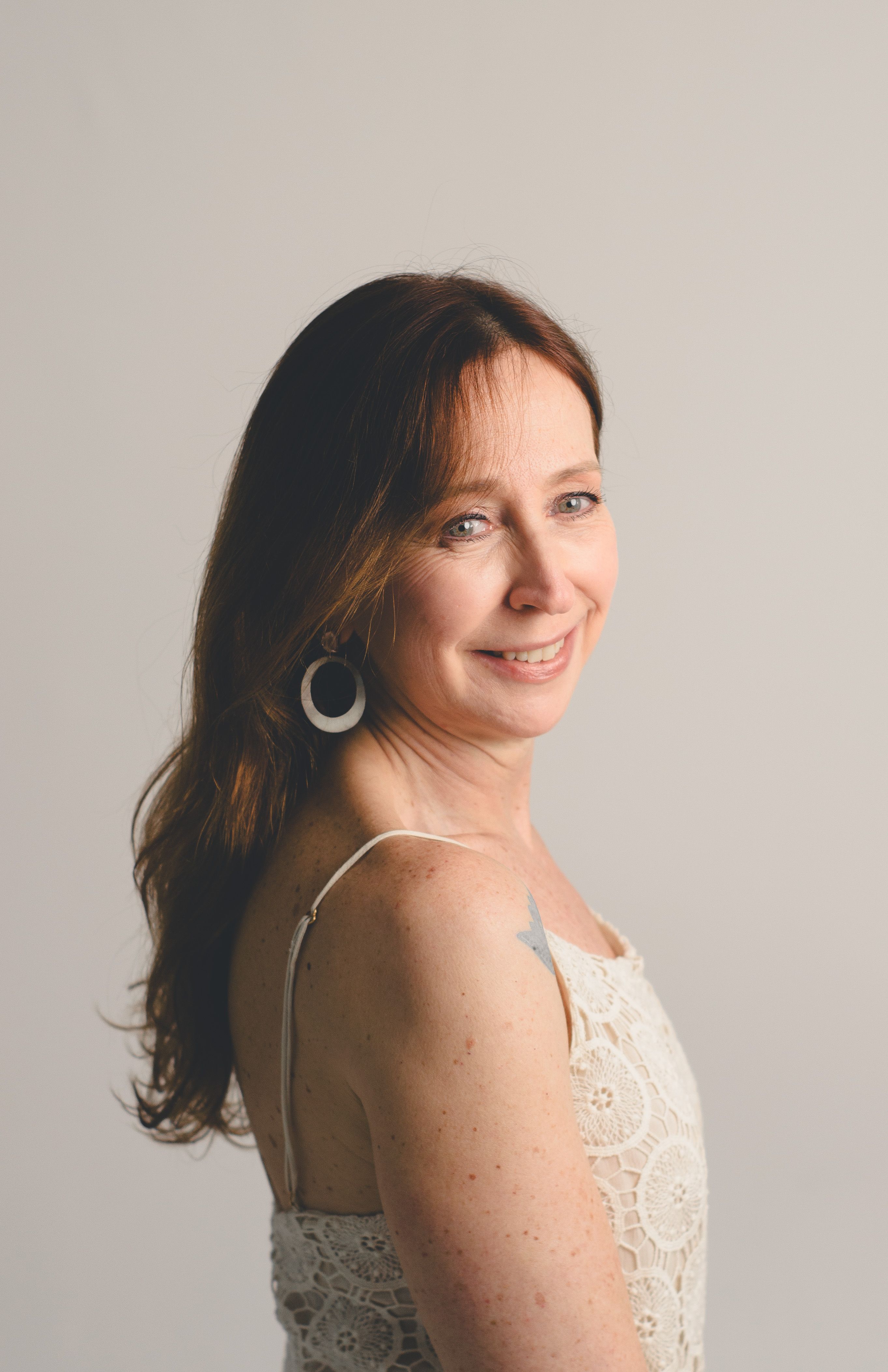 Side profile portrait of a smiling woman with long hair and lace dress.