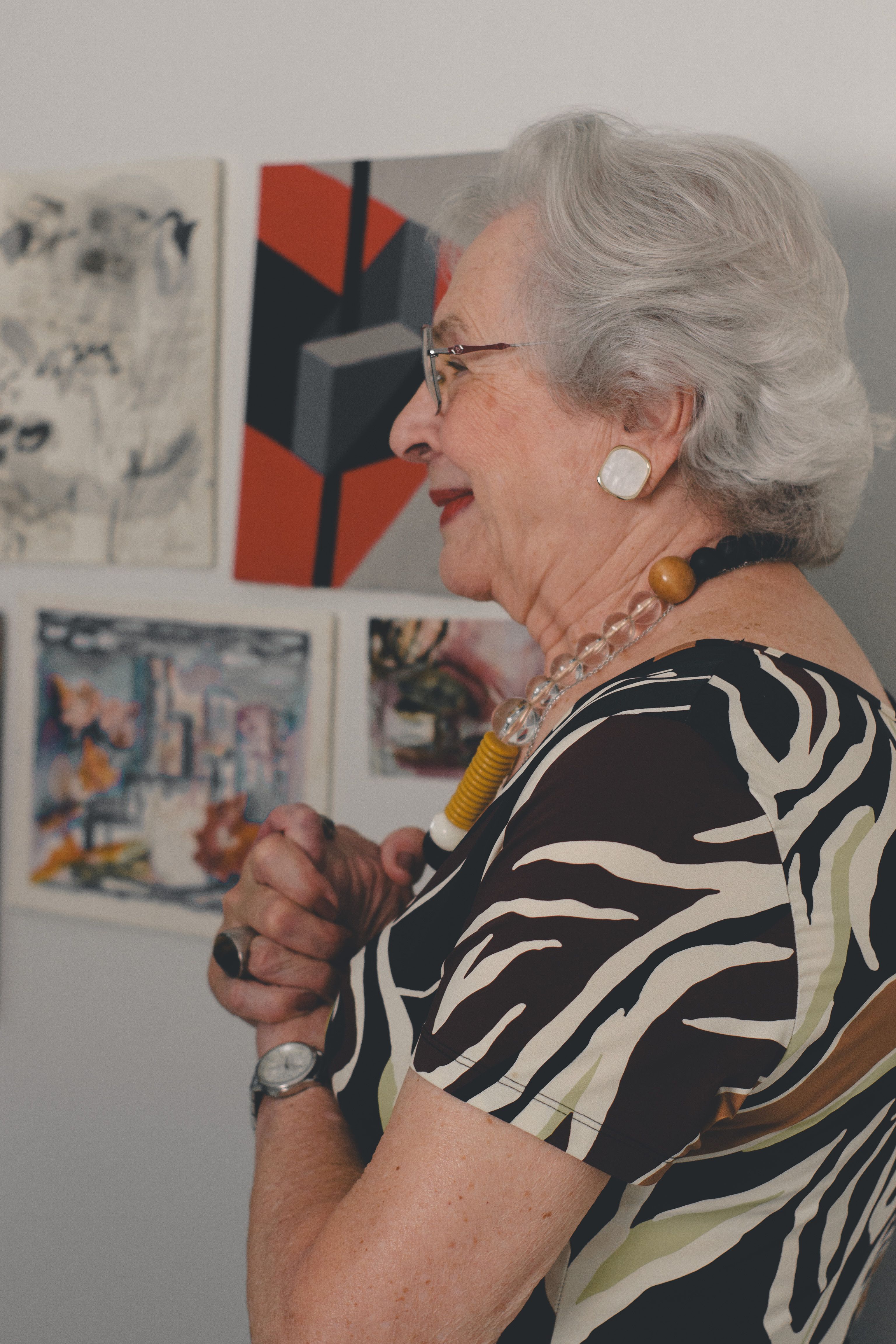 Senior woman observing art in a gallery setting with focus on abstract paintings.