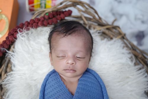 Free A serene baby wrapped in a blue swaddle sleeping peacefully in a nest-like setting. Stock Photo