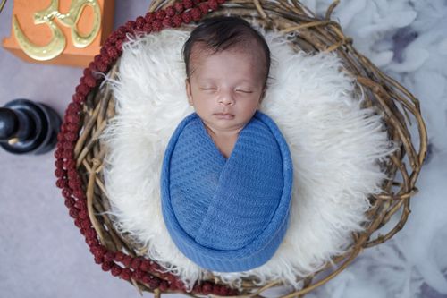 Free A serene newborn baby wrapped in a blue blanket, sleeping in a rustic basket with an Om symbol nearby. Stock Photo