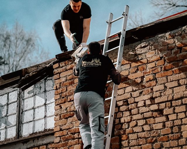 Roofers reaching a building roof Two roofers using a ladder to reach the roof of a brick building