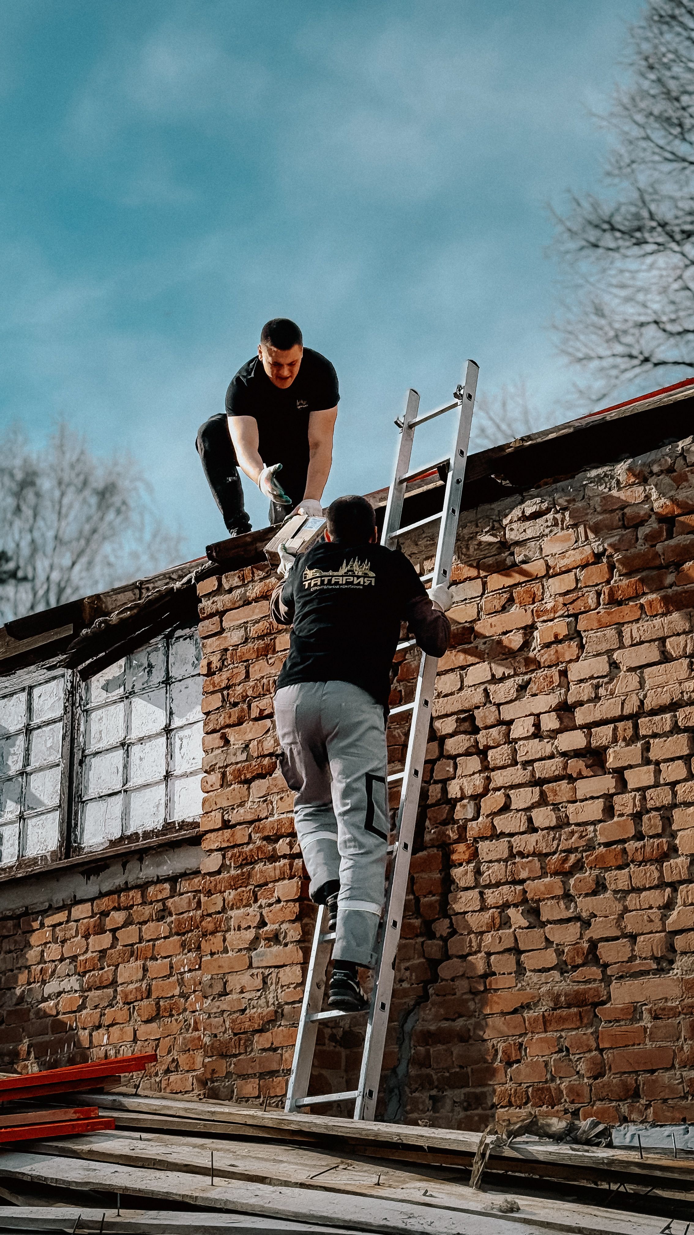 Zadarmo Dvaja stavební robotníci používajúci rebrík na dosiahnutie strechy tehlovej budovy pod modrou oblohou. Fotka z fotobanky