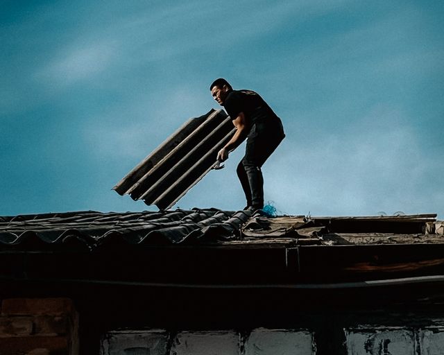 Rooftop repair work Man repairing a rooftop with roofing sheets under a deep blue sky