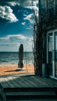 Peaceful seaside scene with a deck and umbrella by a sunny beach, under vivid skies.