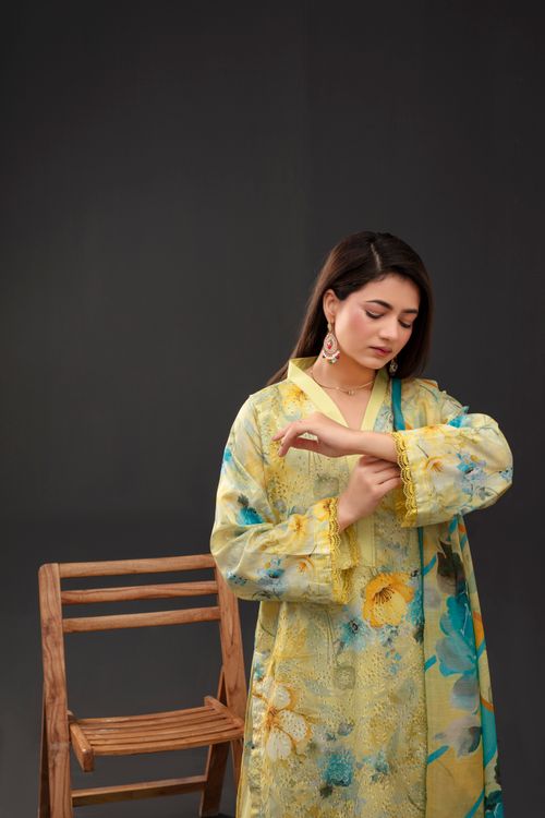 Free A woman in a floral yellow dress stands indoors next to a wooden chair, adjusting her sleeve. Stock Photo