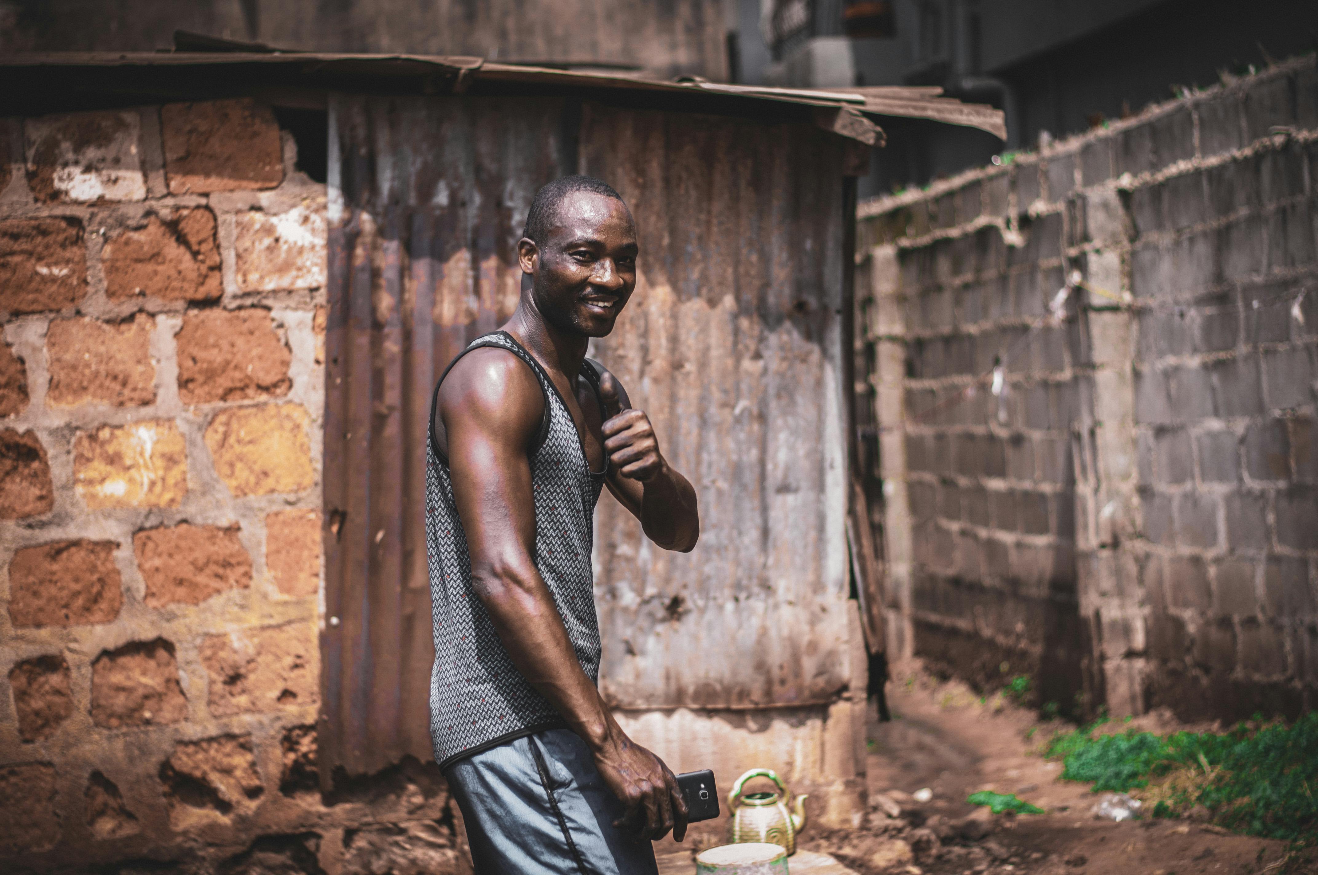一个男人微笑着站在城市街区的砖墙旁，手里拿着智能手机