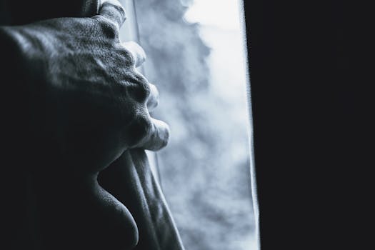 这是一张黑白特写，一只手握住窗帘，光影效果富有戏剧性