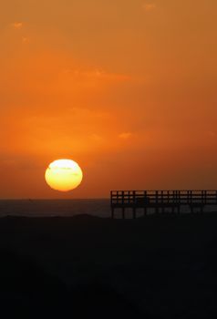 Captivating sunset scene with vivid orange sky and pier silhouette over the ocean horizon. Perfect for travel and nature themes.