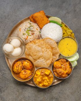 A traditional Indian thali featuring rice, curry, dal, and more, on a brass plate.