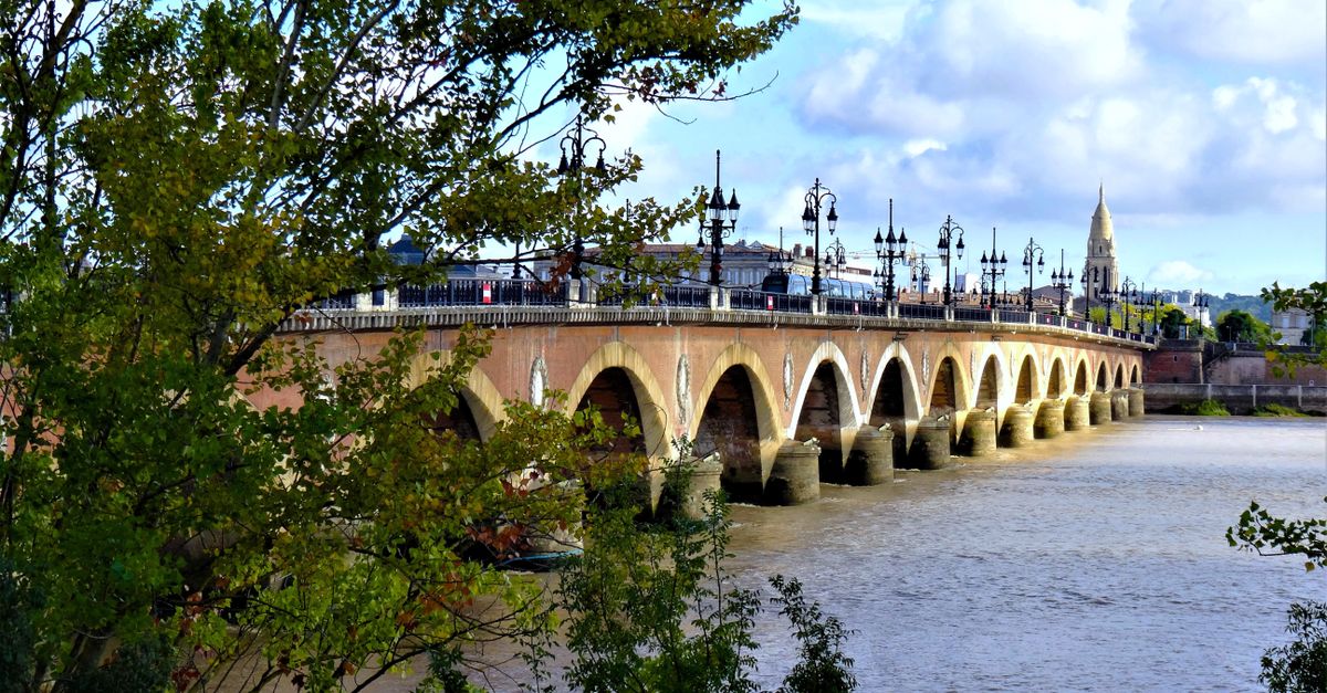 Scenic view of the historic Pont de Pierre bridge over the Garonne River in Bordeaux, France, with clear skies.