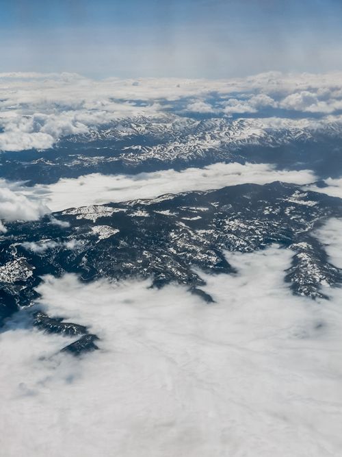 Free Aerial photograph of a snow-covered mountain range peeking through thick clouds. Stock Photo