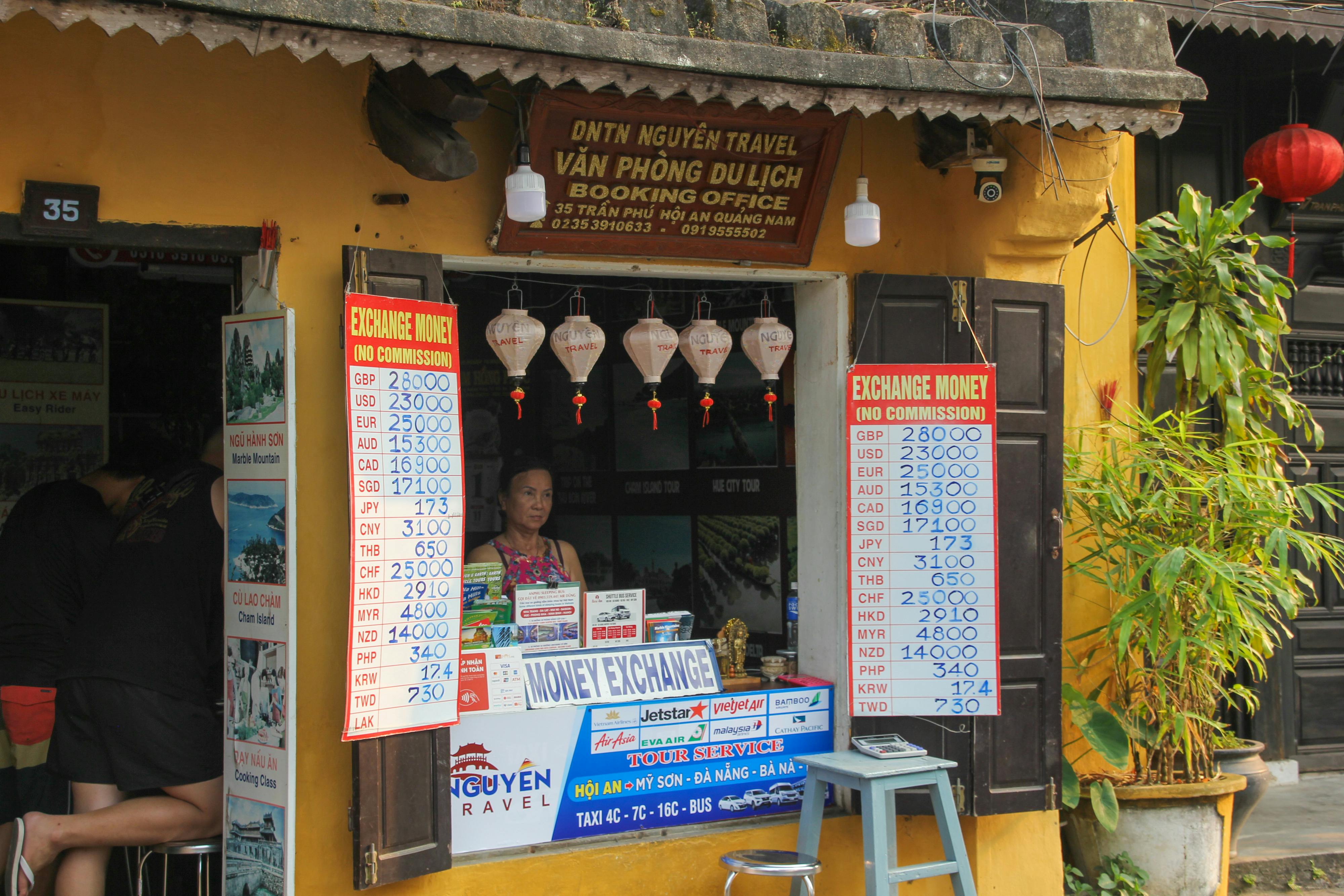 Currency exchange booth in Đà Nẵng, Vietnam, displaying exchange rates. A woman stands inside the office.