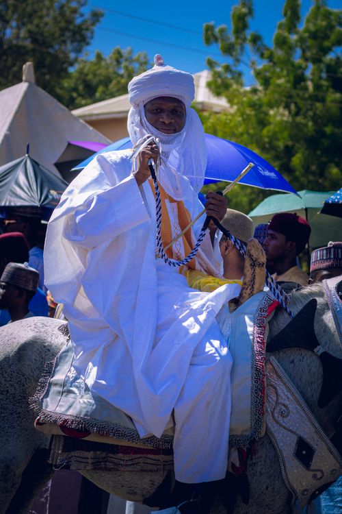 Free African man in white traditional attire on horseback during a vibrant outdoor cultural parade. Stock Photo