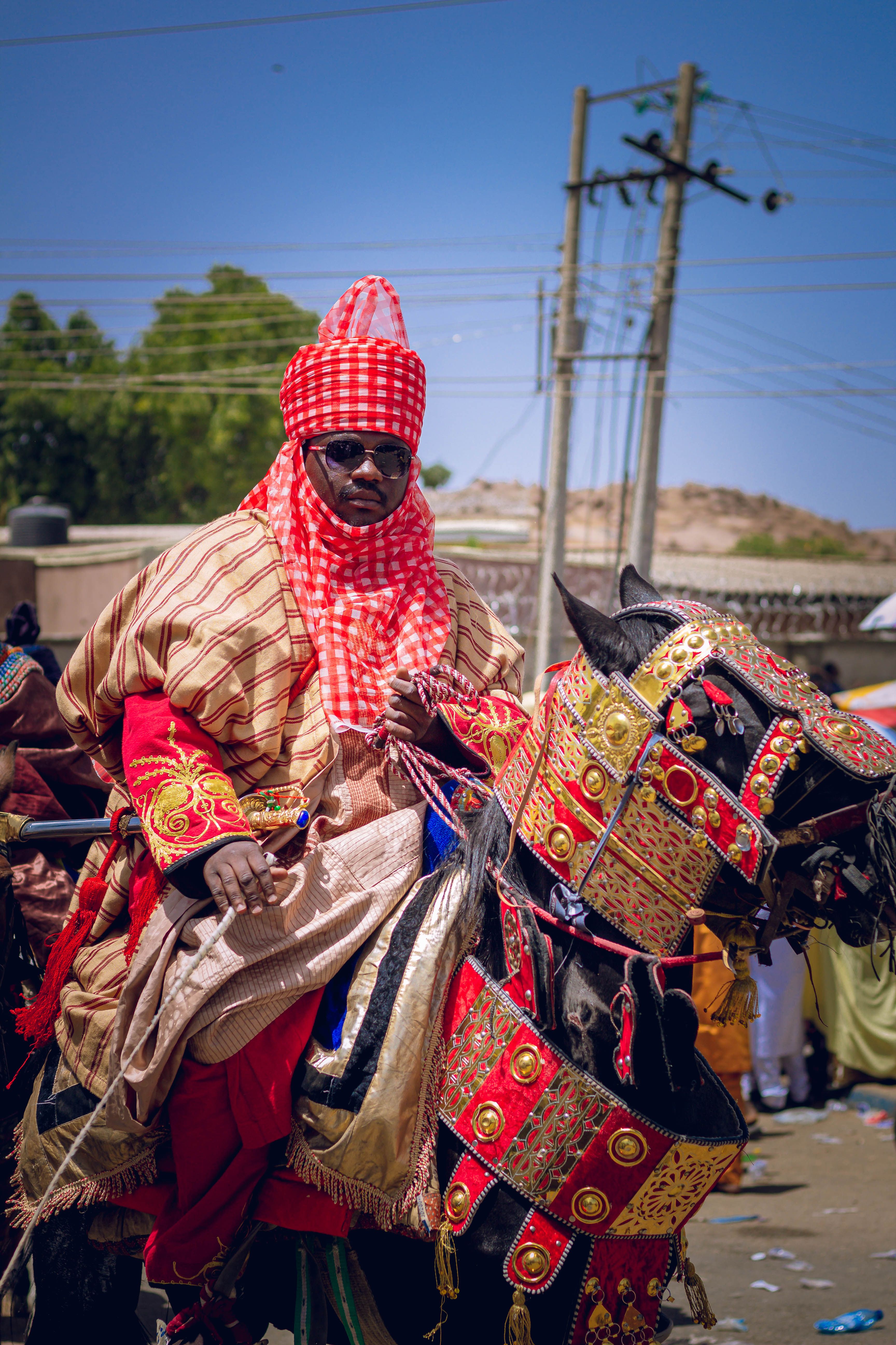 A traditional Nigerian horseman wearing vibrant attire, participating in a cultural parade outdoors.