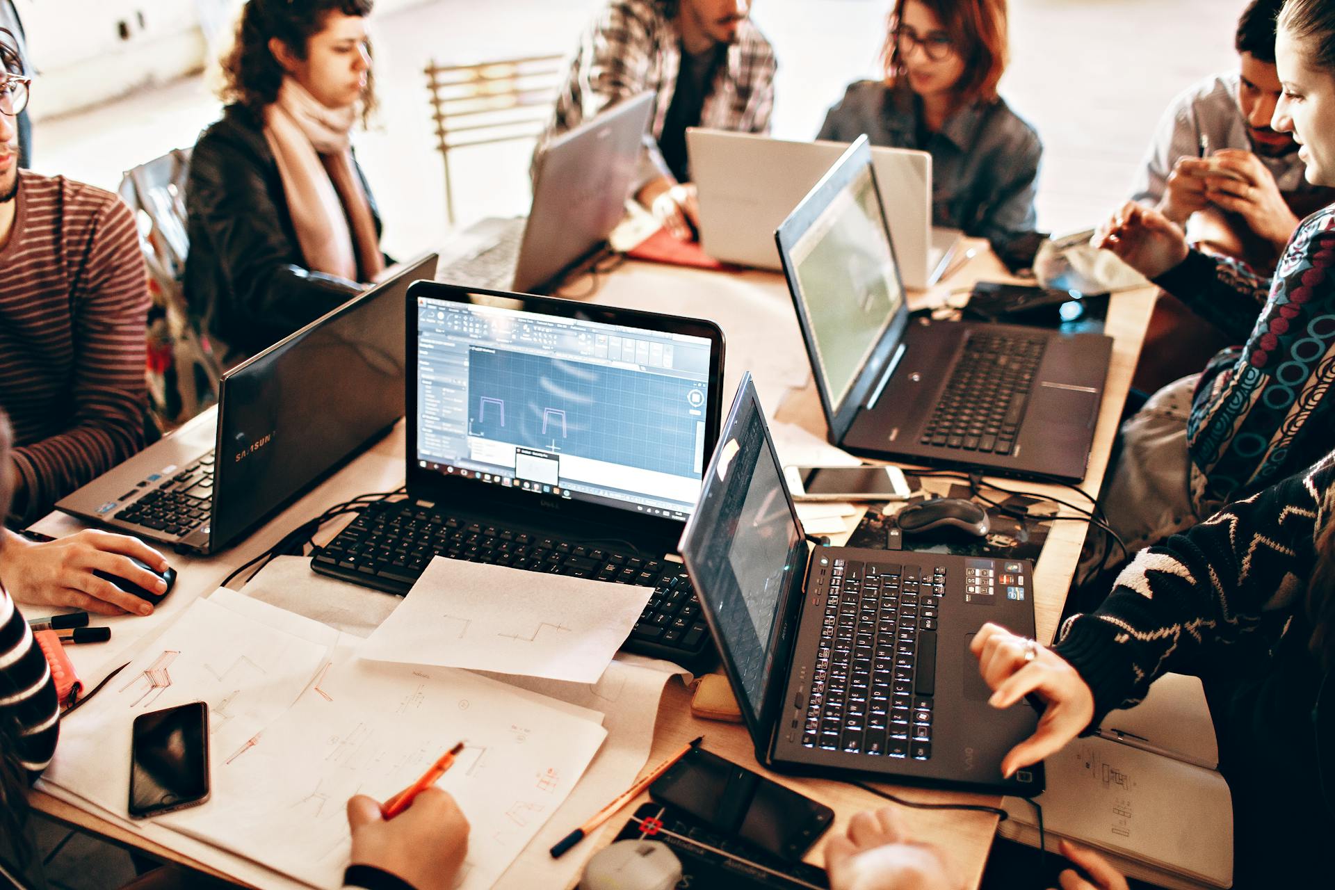 Group of diverse adults collaborating with laptops and papers in a modern office environment.