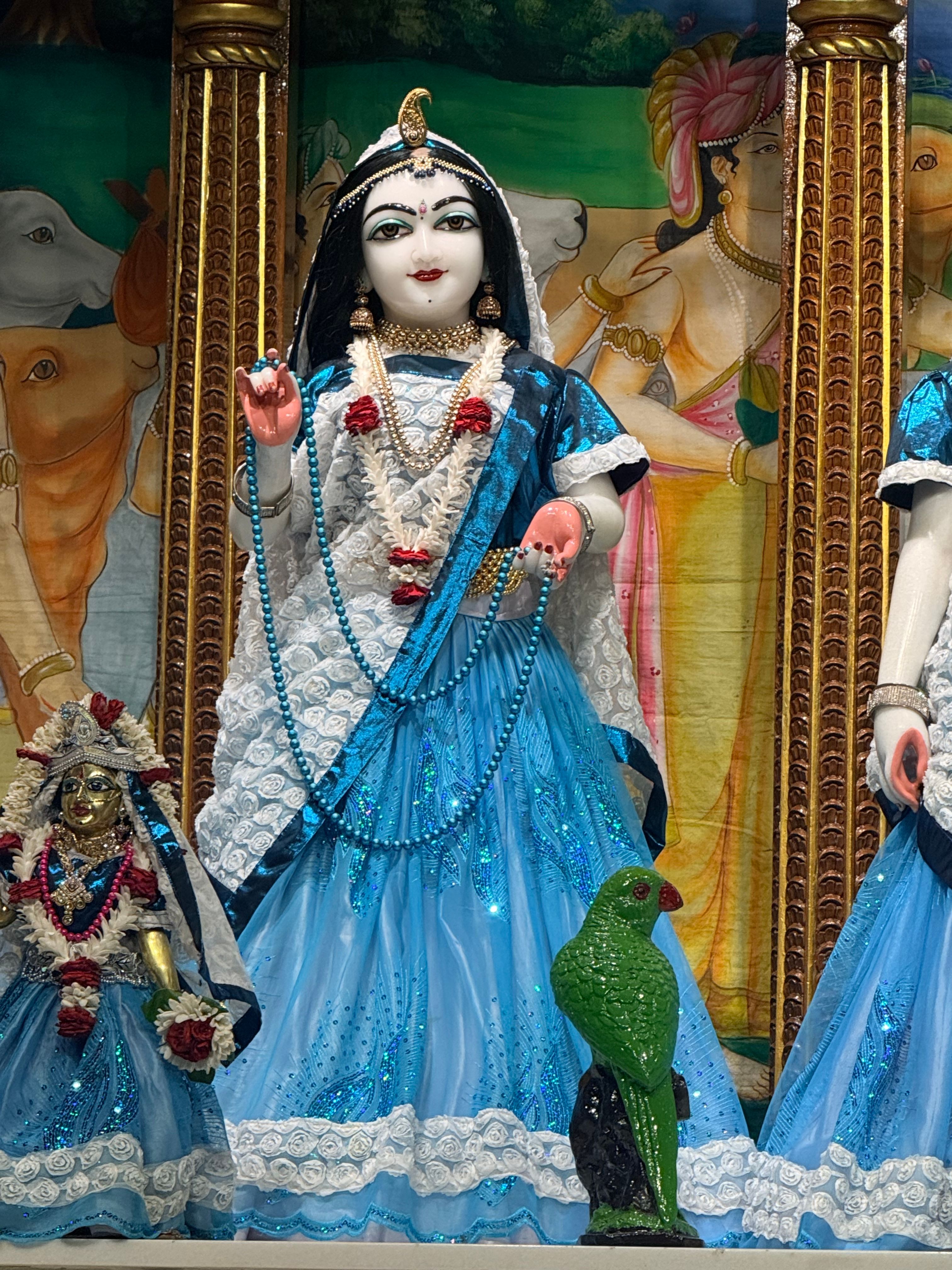Colorful statue of an Indian deity with a parrot in a Tirupati temple, adorned in blue and white attire.
