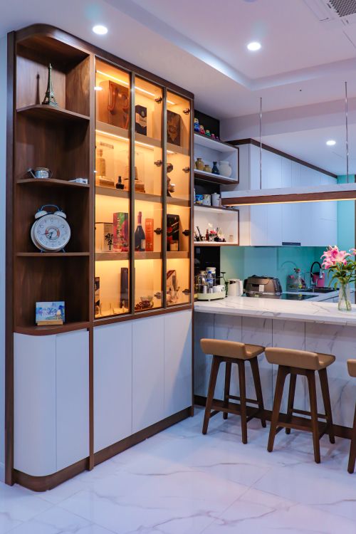 Free A contemporary kitchen featuring illuminated wooden cabinets and marble flooring, complete with bar stools and floral decor. Stock Photo