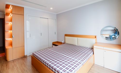 Free Spacious minimalist bedroom featuring a checkered bedspread, wooden furniture, and a modern round mirror. Stock Photo